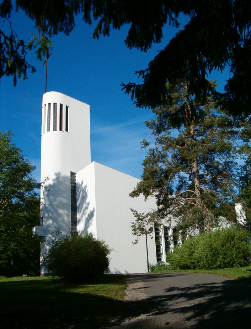 valkoinen korkeatorninen kirkko havupuiden keskellä