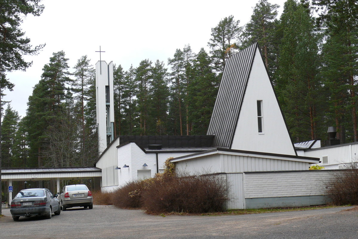 Kolkanlahden siunauskappeli valkoinen rakennus, jossa kolmiomuotoinen torni, taustalla valkoinen korkea kellotorni