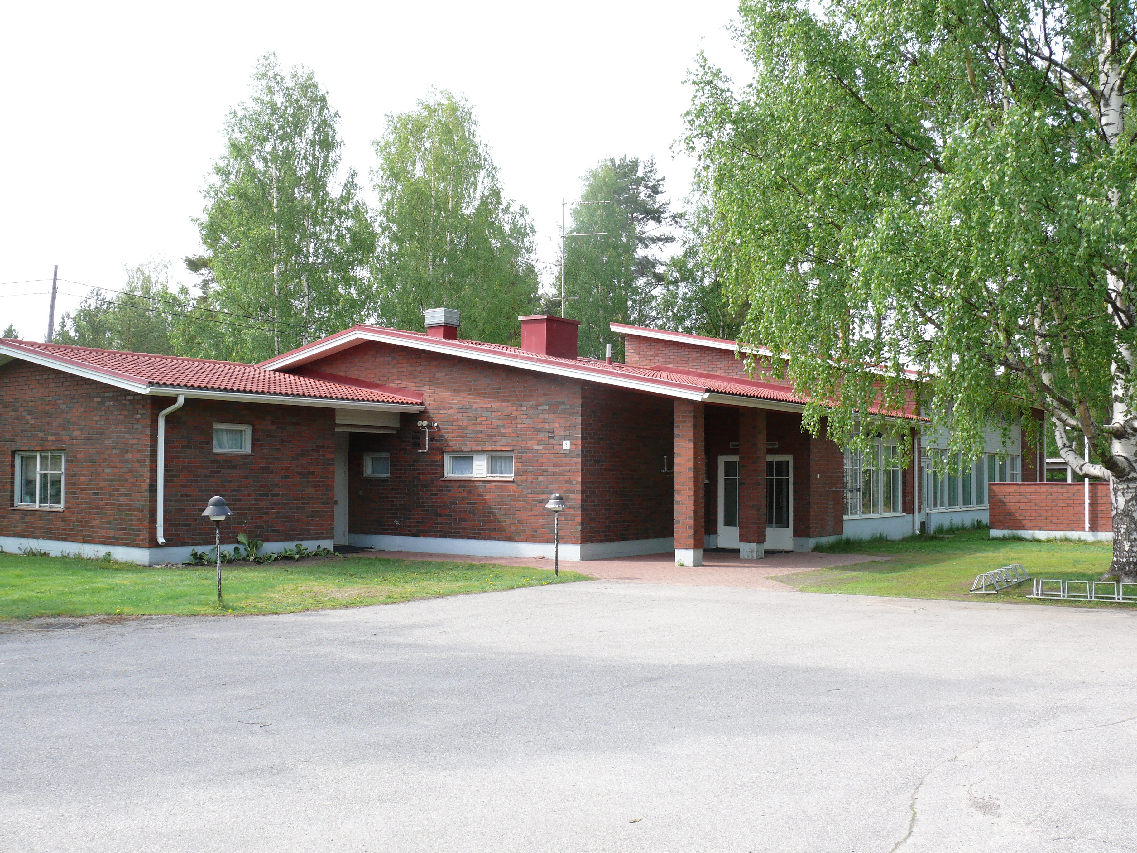 Punatiilinen matala rakennus kesämaisemassa.